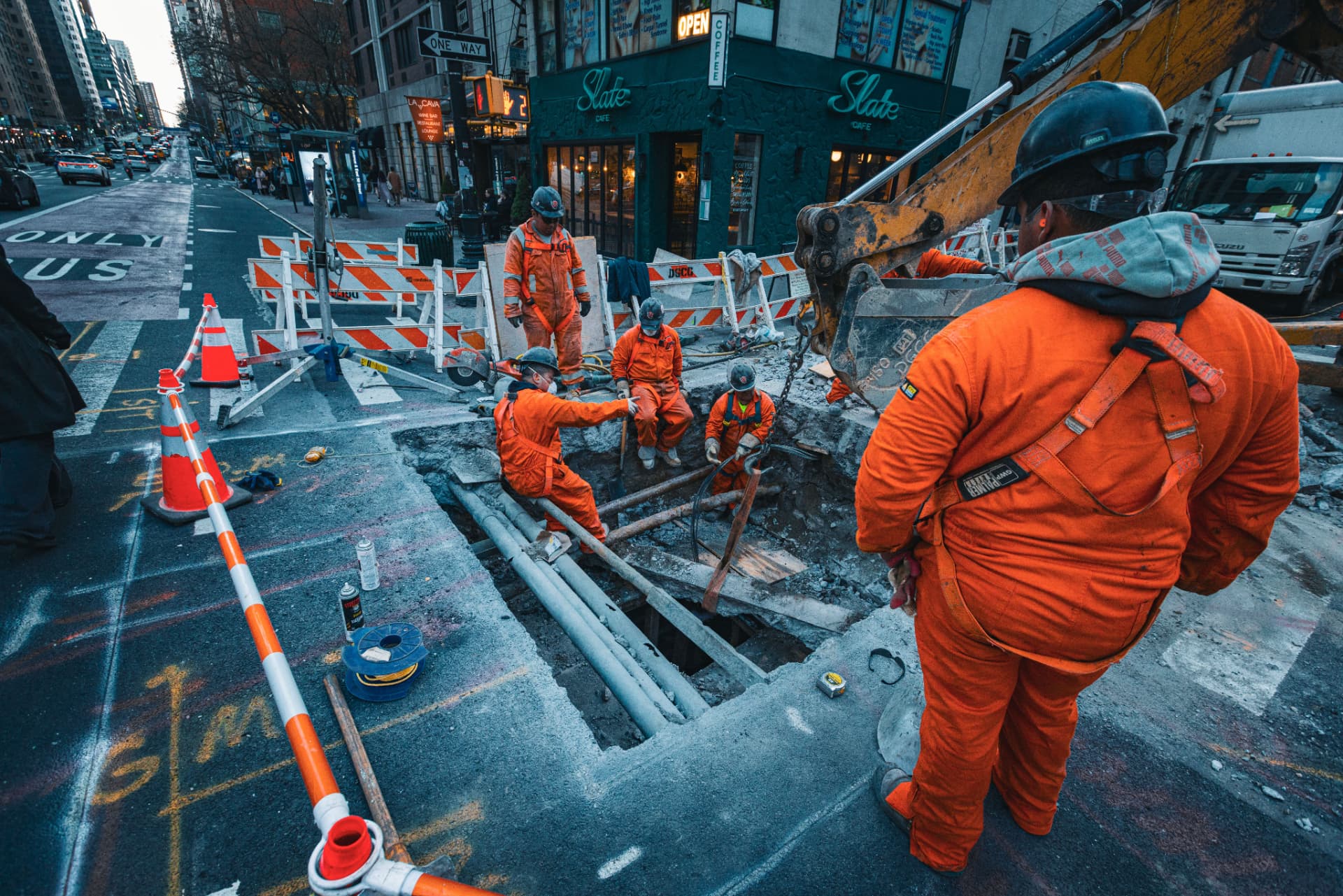 Utility crew in orange safety gear working in an excavated city street